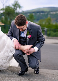 Groom adjusting brides shoe like cinderella outside of wedding venue in Hood River, Oregon.