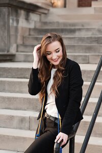 Senior wearing blue and yellow cords at MTSU. Leaning against the banister and laughing shyly