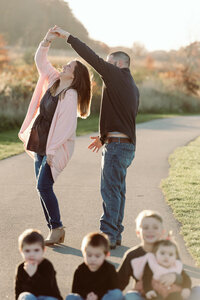 Parents playfully reaching upward together on a path with their children seated in front during a Cleveland family photography session