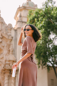 Model in sunglasses and a mauve set walking past ornate architecture, beauty lifestyle frame