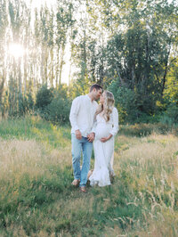 Couple walking hand in hand in a field while sharing a kiss