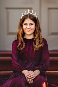 Close up portrait of young girl wearing a purple dress and crown in front of palace doors