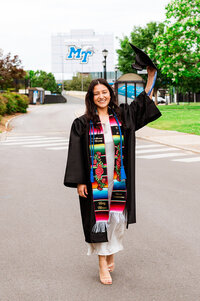 Senior wearing a custom stole walking down the street with the MTSU football stadium behind her