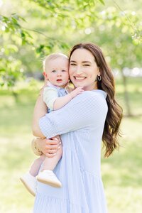 Mother and baby boy smiling at camera under green trees