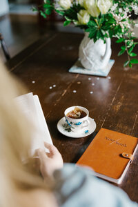 Photo taken over a woman's shoulder of a cup of tea and notebook on a table
