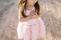 Close-up detail of a young girl from the Parker family wearing a soft pink dress, gently holding her hands together during a natural light family photography session in Las Vegas.