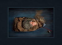 Sleeping newborn posed in a miniature fishing boat with a fishing pole in a fine art portrait inspired by her father's passion for fishing.