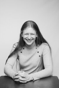 A black and white picture of a long-haired woman laughing in front of a white backdrop.