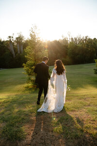 Bride and groom walking hand in hand across sunlit field