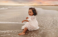 Charleston Baby Milestone Photographer - Toddler delights at the water on the beach during her Baby Milestone Portrait Session in Charleston, SC.