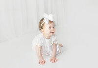 little girl wearing white bow and dress during cake smash photoshoot in Mount Juliet Tennessee photography studio