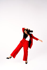 Full-body editorial portrait of business founder in a red suit against a white studio background.