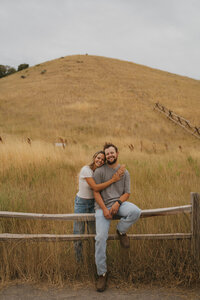 couple sitting on fence during outdoor engagement photoshoot in atlanta