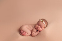 Peaceful newborn baby girl posed on a peach-colored blanket with floral headband during a minimalist newborn session near Waukesha, Brookfield, and Pewaukee.