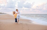 Ponte Vedra portrait session capturing Beach, a husband pulls his wife playfully close while they run through the sand, their footprints trailing behind them along the ocean.