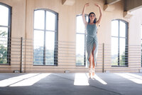 A ballerina stands on point in a parking garage with sunlight streaming through the windows behind her.