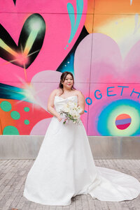 Bride stands in front of NYC mural smiling with her bouquet in hand