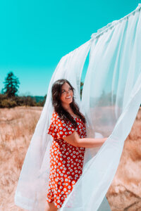 Singer-songwriter in a red floral dress interacting with flowing fabric during an outdoor editorial photoshoot