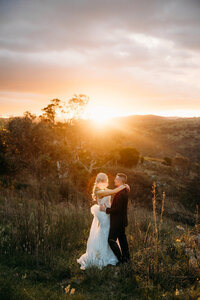 Sunset wedding photos at Brindabella Hills Winery. Couple hold each other and look over to the sunset across the Murrumbidgee River