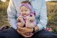 a baby holds her feet while in her dad's arms