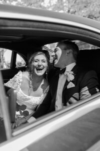 A couple smiles from a car on their wedding day