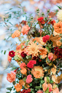 A close-up of the flowers on the chuppah, with red and peach roses, golden dahlias, and deep burgundy blooms reaching toward the clear blue sky.
