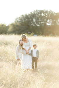 A mother and 2 children holding hands as they walk though a field at a local Dallas park.
