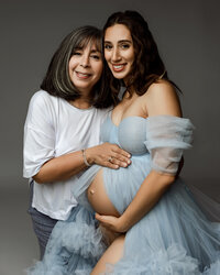 Close-up of a pregnant mom and her mother smiling together, hands resting on the baby bump during a maternity photoshoot in Yucaipa by Kaitlyn Dawn Photography.