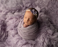 Sleeping newborn baby girl wrapped in a lavender swaddle and posed on a soft purple flokati blanket during a studio newborn photography session with newborn photographer Kaitlyn Dawn Photography.