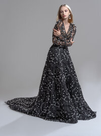 Model in a black gown with sheer sleeves and a celestial pattern, full train spread across a grey studio floor.