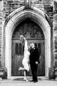 Bride kicking up her heel and holding up a bouquet after eloping at Scarritt Bennett Center in Nashville. Photo is in black and white.