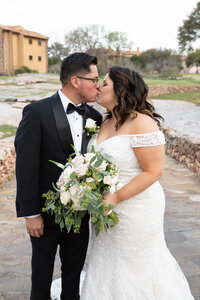 A bride and groom sharing a romantic kiss in front of a stone walkway captured beautifully by an Austin wedding photographer.