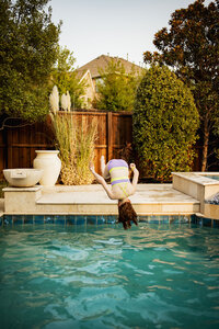 A girl does a flip into the pool in the backyard