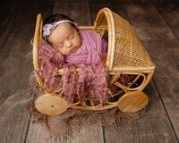 Sleeping newborn baby girl wrapped in a dusty rose swaddle and posed in a vintage wicker stroller prop during a studio newborn photography session in Inland Empire by Kaitlyn Dawn Photography.