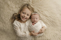 Two sisters dressed in white at a newborn studio session.