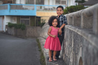 Brother and sister standing together along stone wall during city family photography session