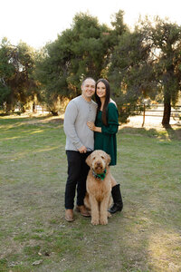 Couple standing together with their dog in a natural outdoor setting, warm sunset lighting photographed by Kaitlyn Dawn Photography, professional family photographer.