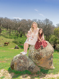 Orange County family photography of a mother and her two daughters sitting on a rock in a happy candid moment with true to life color and soft natural light.