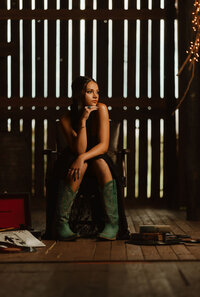 Senior portrait at Triple T Farms in Fruitdale, Alabama — sitting in a leather chair in an elegant
black dress and teal cowboy boots.