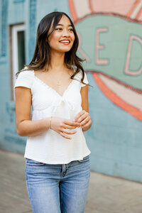 High school senior girl smiling in front of a mural wearing a white top and jeans, senior portrait session by Kaitlyn Dawn Photography.