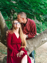 Man kissing his girlfriend on the forehead under a tree during a romantic engagement photo session in a Los Angeles park.
