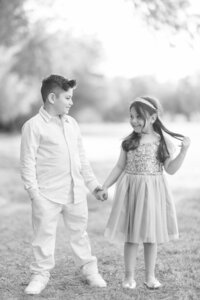Black and white portrait of two Dilorio children holding hands and smiling at each other in an outdoor Las Vegas setting during a sibling photography session.
