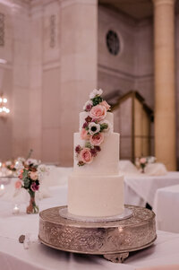 White wedding cake with pink and purple florals prior to being cut