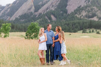 A family of four laugh together while posing in front of the flat irons at Chautauqua park in Boulder.