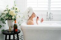Women entrepreneur in a bubble bath applying lipstick during a photography session.