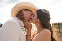 Groom in a white cowboy hat kissing his bride at sunset during their wedding