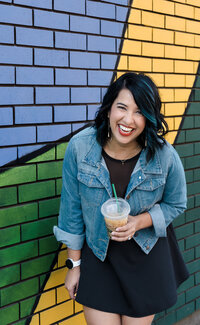 brand photo of a woman with a cup of coffee laughing close to a colorful mural in Sacramento
