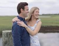 Couple in blue shirt and floral dress embrace on dock on Nantucket Island.