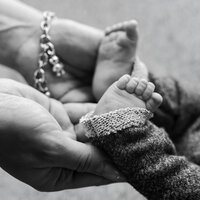Black and white close-up of a newborn baby's tiny feet resting in a parent's hands during an intimate newborn photography moment captured by Kaitlyn Dawn Photography.