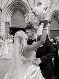 Classic black and white wedding exit photo of a bride and groom kissing outside a cathedral after their Dayton Arcade wedding.